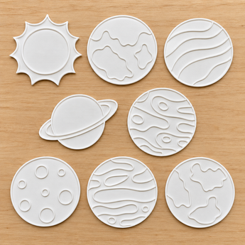 Eight white 3D-printed space coloring pieces including planets, a sun, a moon, and a ringed planet